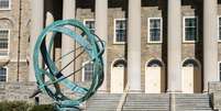 Um relógio de sol de metal no campus da Universidade Estadual da Pensilvânia, com o prédio Old Main ao fundo, um marco local em State College, Pensilvânia, EUA.  Foto: Getty Images / BBC News Brasil