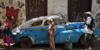 Imagem de arquivo. Pessoas passam por um carro com pneu furado em Havana Velha, Cuba, em 6 de janeiro de 2026. Pa&iacute;s sofre com acelera&ccedil;&atilde;o de crise demogr&aacute;fica.  Foto: &copy; Ramon Espinosa / АР / RFI