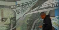 Um homem passa em frente a uma casa de c&acirc;mbio, com adesivos de notas de d&oacute;lar na porta e nas paredes  Foto: Reuters