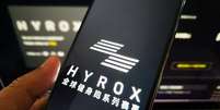 Mulher segura um telefone celular mostrando a marca Hyrox  Foto: Getty Images / BBC News Brasil
