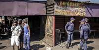 Policiais sul-africanos cercam um estabelecimento onde dez pessoas morreram em um tiroteio na madrugada deste domingo (27), no munic&iacute;pio de Lwandle, nos arredores da Cidade do Cabo.  Foto: AFP - GIANLUIGI GUERCIA / RFI