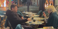 Casal toma drink perto de lixeira em chamas durante protestos em Paris  Foto: Reprodução