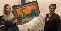 Policiais seguram o quadro O Sol Poente ap&oacute;s recuper&aacute;-lo de furto em 2022, antes de a obra ser oferecida a Vorcaro Foto: Reuters / BBC News Brasil