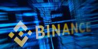 O logotipo da Binance, que sofreu um ataque hacker,  em contraste com um texto azul desfocado, típico de computador.  Foto: Reuters / BBC News Brasil