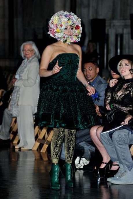 Web Gaga acaparó todas las miradas en la primera jornada de la Semana de la Moda de Londres. La cantante, gracias a sus excéntricos looks, dejó en segundo plano a los diseñadores de la pasarela londinense. Gaga desfiló para el diseñador Philip Treacy con una capa rosa flúor que cubría todo su cuerpo. Al ser semitransparente, se pudo ver que debajo llevaba puesto un ajustado mono color carne flores estampadas. Minutos antes del desfile, la cantante lució un vestido de terciopelo verde y leggins doradas. Pero todas las miradas se desviaban a su cabeza, en la que llevaba una corona de flores que le cubría toda la cara. También se la vio con unas enormes orejas de Minnie Mouse con incrustaciones de pedrería que hacían juego con su camisa, encima de la que llevaba una chaqueta blanca decorada con perlas. Esto no fue todo, Lady Gaga sorprendió al público londinense con un último cambio de vestuario: un modelo turbante que incluía pieles colgantes.