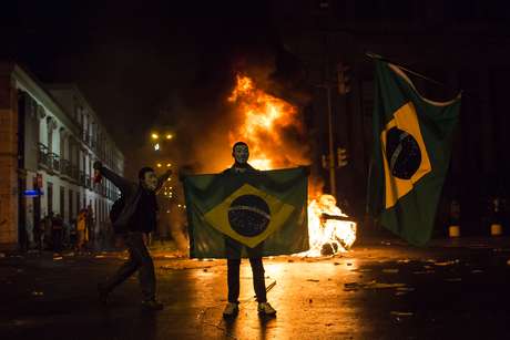 Mascarado, manifestante mostra a bandeira do Brasil em frente a uma barricada de lixo em chamas no Rio de Janeiro <p>Mascarado, manifestante mostra a bandeira do Brasil em frente a uma barricada de lixo em chamas no Rio de Janeiro</p>