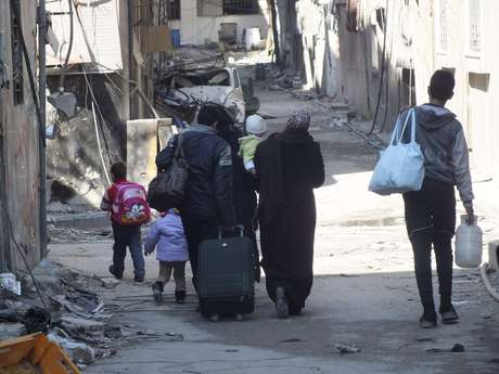 Civis levam seus pertences enquanto caminham até um ponto de encontro para serem evacuados da zona citiada de Homs Civis levam seus pertences enquanto caminham até um ponto de encontro para serem evacuados da zona citiada de Homs