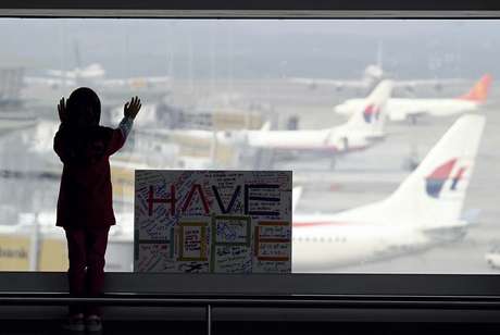 AP Menina observa os aviões, ao lado de uma placa que diz "temos esperanças", colocada no aeroporto internacional de Kuala Lumpur, na Malásia, nesta segunda-feira, 10 de março