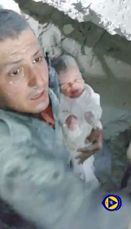 Homem sorri apertando o bebê em seus braços, enquanto gritos de "Deus é grande" ecoam atrás da câmera <p>Homem sorri apertando o bebê em seus braços, enquanto gritos de "Deus é grande" ecoam atrás da câmera</p>