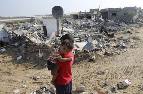 Menino palestino carrega o irmão no colo em frente aos destroços da casa da família em Gaza, em 13 de agosto Menino palestino carrega o irmão no colo em frente aos destroços da casa da família em Gaza, em 13 de agosto