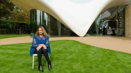 Zaha Hadid em frente a um de seus projetos com as curvas características de seu estilo