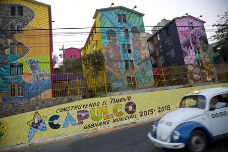 En esta foto del 11 de mayo de 2016, un taxi pasa por la unidad de viviendas Cuauhtémoc, cerca de un mensaje de propaganda local, en la ciudad turística de Acapulco, estado de Guerrero, en México. La más reciente oleada de homicidios comenzó el 24 de abril con tiroteos a lo largo de la avenida costera en la ciudad, de 800.000 habitantes. Acapulco tenía una tasa de homicidios de 146 personas por cada 100.000 habitantes en 2012. La tasa ha bajado a unos 112 por 100.000 pero rebasa por mucho las de otras ciudades del país.