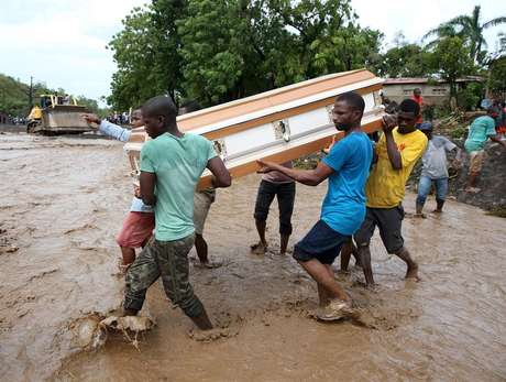 EFE Homens carregam caixão e tentam atravessar o rio La Digue após a derrubada da única ponte pelo furacão Matthew