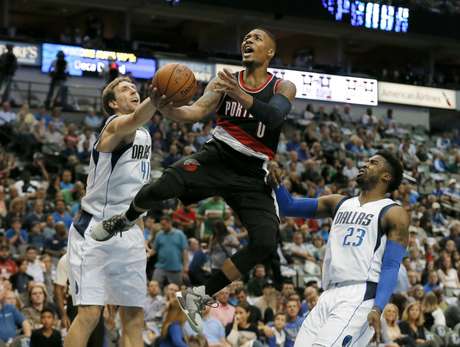 El base de los Trail Blazers de Portland, Damian Lillard. realiza un disparo tras dejar atrás a los aleros de los Mavericks de Dallas Dirk Nowitzki y Wesley Matthews