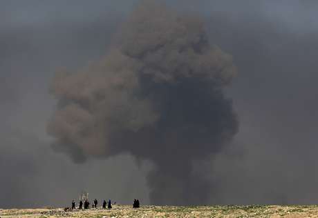 ARCHIVO - En esta imagen de archivo del 9 de marzo de 2017, una gran nube de humo se alza durante los combates entre fuerzas de seguridad iraquíes y milicianos del grupo extremista Estado Islámico, mientras varios civiles caminan hacia terreno controlado por las fuerzas de seguridad iraquíes tras huir de sus hogares en el lado occidental de Mosul, en Irak.