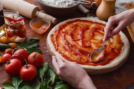 Molho de tomate sendo espalhado pela massa da pizza