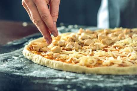 Ingredientes do recheio sendo adicionados à pizza