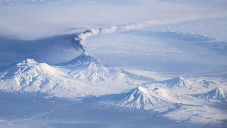 O Udina é um dos vulcões da Península Kamchatka, na Rússia, e fica próximo de outro vulcão ativo, o Kliuchevskoi (visto nesta foto com uma coluna de fumaça)