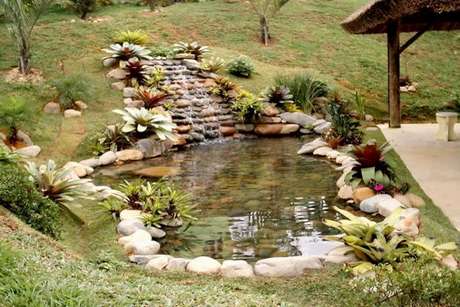 2. O lago artificial decorado com pedras e uma pequena cascata adornada de flores foi feito para encantar a área externa casa sem atrapalhar a passagem – Por: Ideia de casa