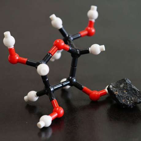Um pedaço do meteorito Murchison ao lado do que seria a estrutura molecular da ribose, um dos açúcares encontrados em sua poeira Um pedaço do meteorito Murchison ao lado do que seria a estrutura molecular da ribose, um dos açúcares encontrados em sua poeira