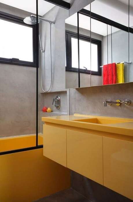16. Modelo de banheiro de apartamento moderno com paredes de cimento queimado e banheira e gabinete amarelos – Foto: Archdaily 16. Modelo de banheiro de apartamento moderno com paredes de cimento queimado e banheira e gabinete amarelos – Foto: Archdaily