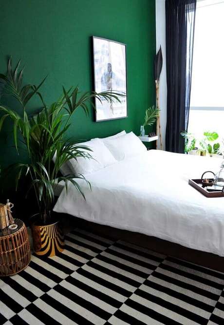 36. Parede verde escura para decoração de quarto com tapete listrado preto e branco e vasos de plantas – Foto: Apartment Therapy
