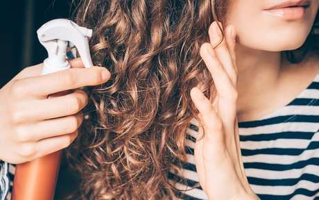 Mulher aplicando produto no cabelo cacheado