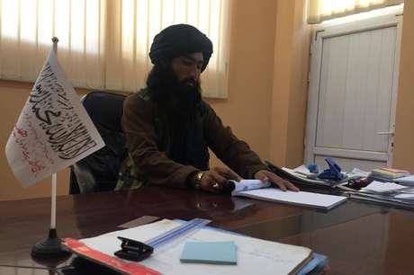Prefeito do Talebã em Bactro em sua mesa de madeira, com uma pequena bandeira branca do "Emirado Islâmico do Afeganistão"