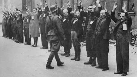 Um soldado da SS, a milícia nazista, aborda trabalhadores judeus no gueto de Varsóvia em 1943 Um soldado da SS, a milícia nazista, aborda trabalhadores judeus no gueto de Varsóvia em 1943