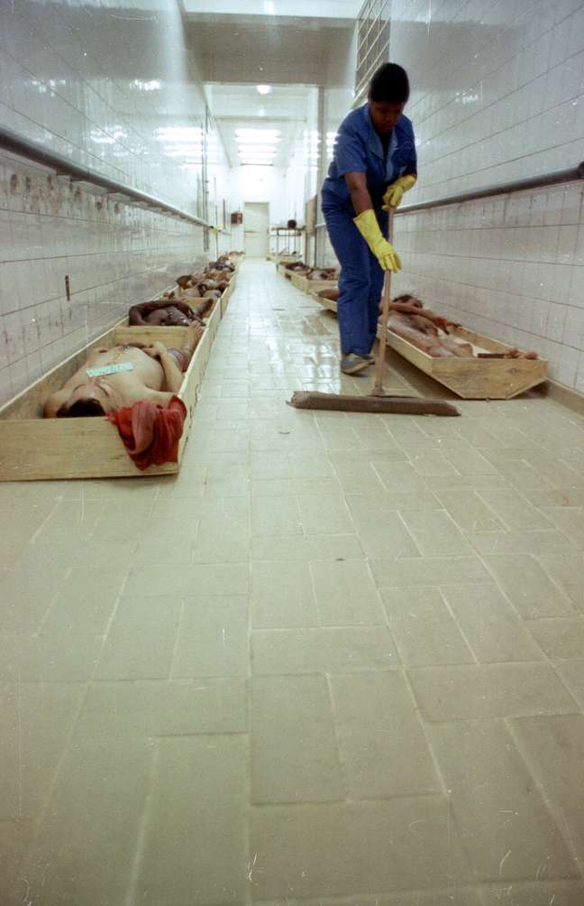 <p>Faxineira limpa o chão de corredor do IML enquanto os corpos dos detentos mortos são acondicionados em caixas de madeira</p>