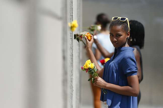 Sasha coloca uma flor no memorial montado com uma parte do Muro de Berlim