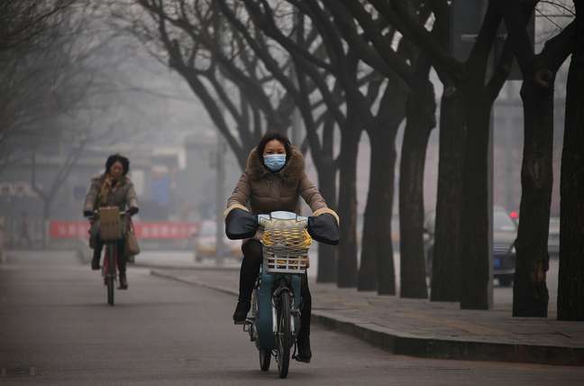 <p>Mulher usa máscara enquanto anda de bicicleta durante tarde encoberta, em Pequim. Pesquisadores foram enviados às partes mais atingidas pela poluição para tentar conter as densas nuvens de poluentes que já cobriram 15% do país</p>