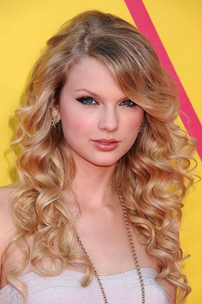 A cantora Taylor Swift usa cachos largos com franjão jogado para o lado 