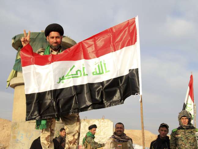 <p>Soldado iraquiano ergue símbolo de vitória próximo à bandeira nacional em Tikrit, Iraque</p>