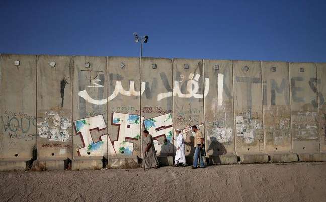 Palestinos passam pelo controverso muro israelense a caminho da primeira oração do período sagrado do Ramadã, no posto de controle de Qalandia, perto de Ramallah, na Cisjordânia, nesta sexta-feira. 19/06/2015