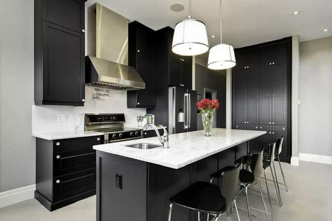 6. Cozinha decorada com pendentes sobre a ilha e com armário de cozinha preto planejado e com bancada branca.