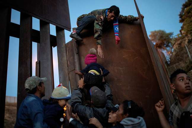 Imigrantes de Honduras que fazem parte de caravana a caminho dos EUA pulam cerca na fronteira do México com os EUA na cidade mexicana de Tijuana