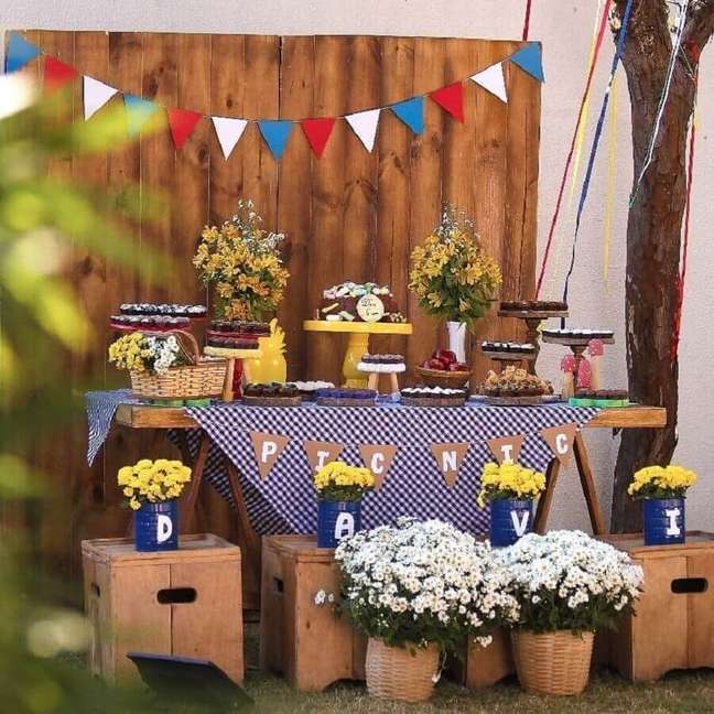 20. Arranjo de flores e toalha xadrez azul para aniversário piquenique com móveis de madeira – Foto: Vila Afetiva Festas
