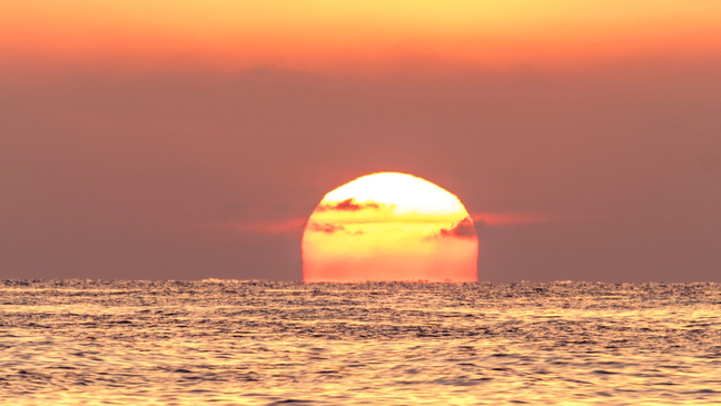O sol pode ficar vermelho sobre o mar e com um céu laranja.