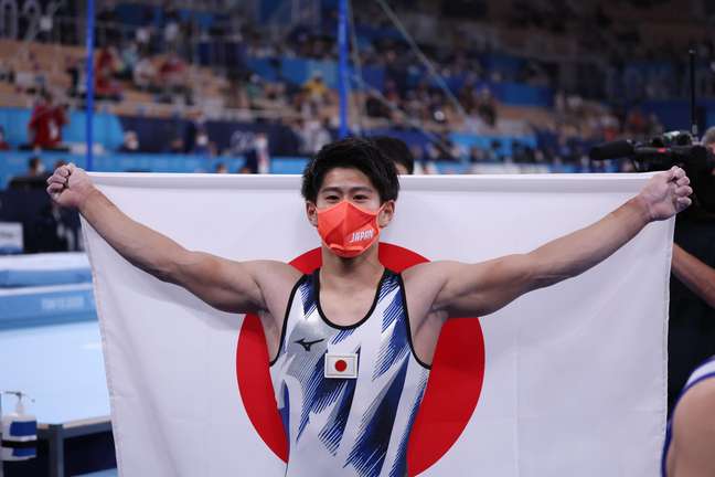 Daiki Hashimoto exibe a bandeira do Japão após faturar medalha de ouro na ginástica