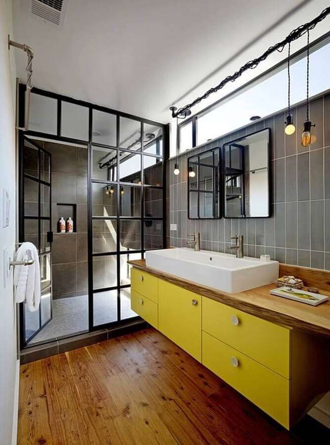 14. Banheiro industrial decorado com gabinete amarelo e bancada de madeira – Foto: Robert Nebolon Architects
