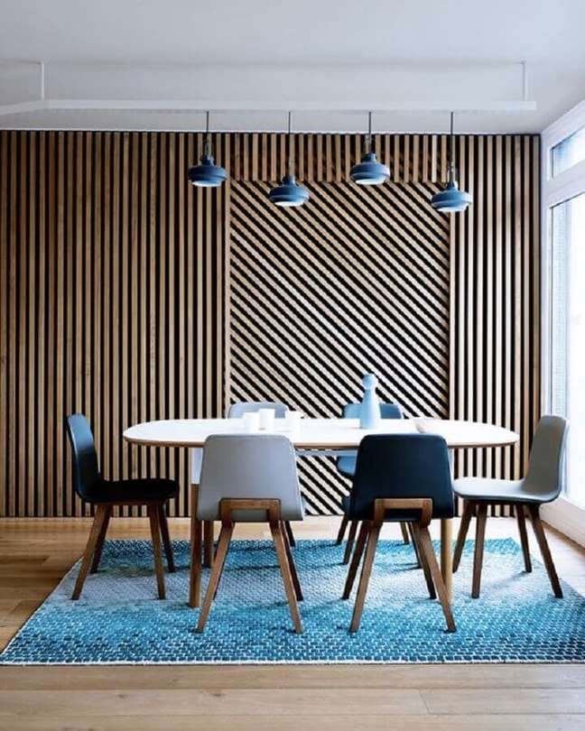 42. Parede ripada de madeira para sala de jantar decorada com tapete e cadeiras azuis – Foto: Decor Fácil