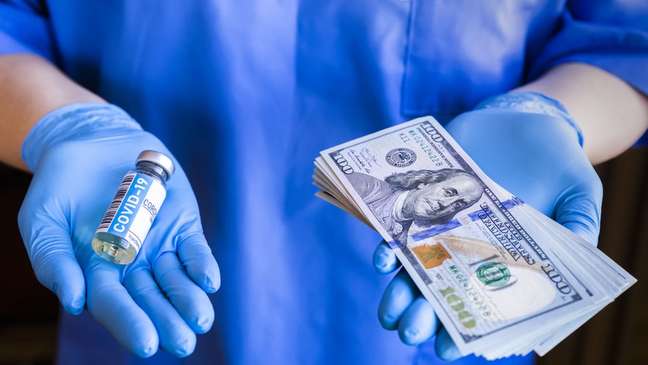 Ampola de vacina em uma mão e notas de dinheiro na outra