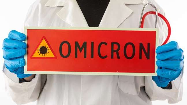 Pessoa com luva segura placa em que se lê: ômicron Pessoa com luva segura placa em que se lê: ômicron