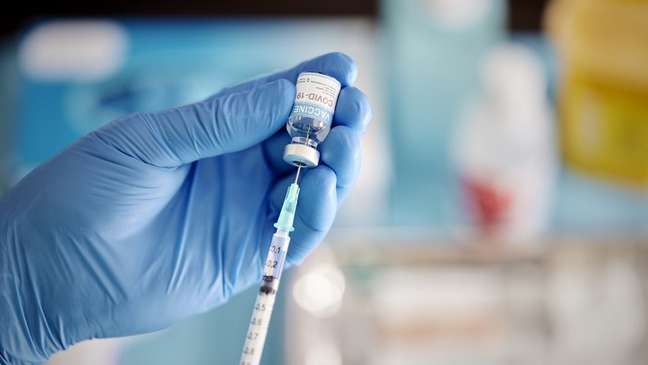 Pessoa de luva retira vacina da ampola com seringa