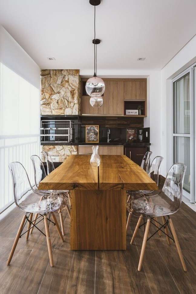 16. Cadeira transparente para espaço gourmet pequeno decorado com mesa de madeira e parede de pedra – Foto: Idealizzare Arquitetos – Consultoria em Projetos