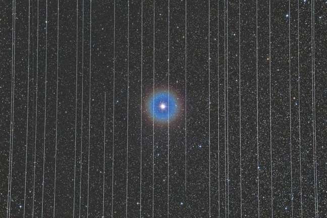 Foto "A Prisão da Tecnologia", vencedora do prêmio de Fotografia Astronômica de 2020; a estrela binária Albireo, na constelação de Cisne, atrás das "grades" de diversos rastros dos satélites da Starlink 