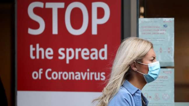 Uma mulher usa uma máscara facial e uma placa diz 'pare a propagação do coronavírus'