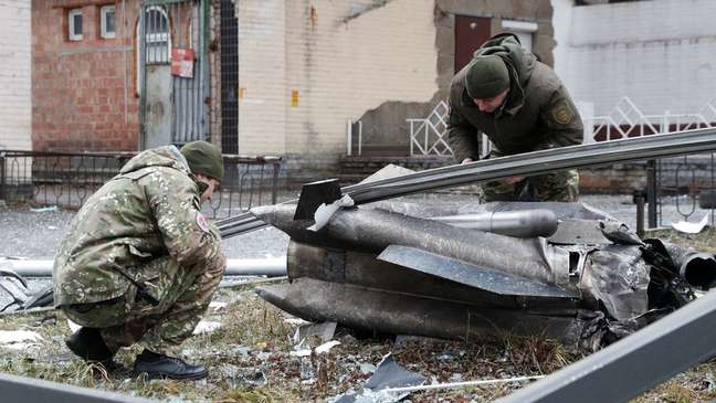 Policiais inspecionam fragmentos de um míssil que caiu numa rua da capital Kiev, logo após Putin determinar a invasão da Ucrânia