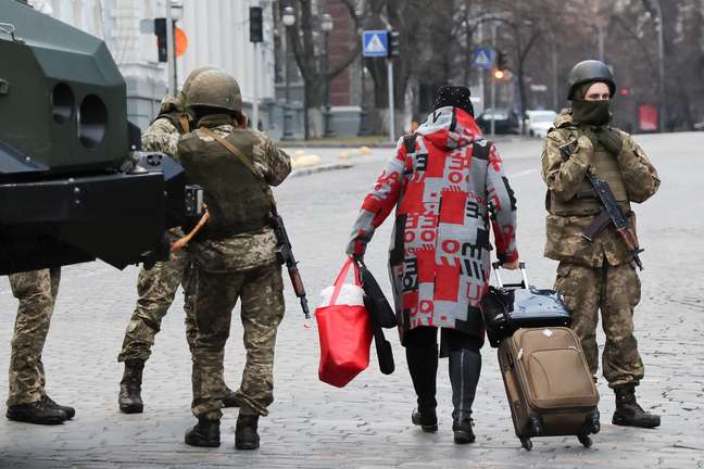 Uma mulher passa por militares ucranianos que guardam uma estrada que leva a um bloco do governo, depois que o presidente russo, Vladimir Putin, autorizou uma operação militar no leste da Ucrânia, em Kiev, Ucrânia, em 24 de fevereiro de 2022